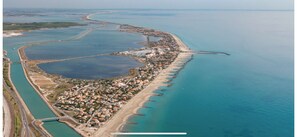 Vista aerea di una cittadina costiera con una lunga spiaggia, un porto turistico e una strada che costeggia la costa.