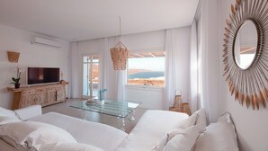 Moderni hotellihuone, jossa on suuri sänky, lasinen sohvapöytä, televisio ja näkymä merelle.
