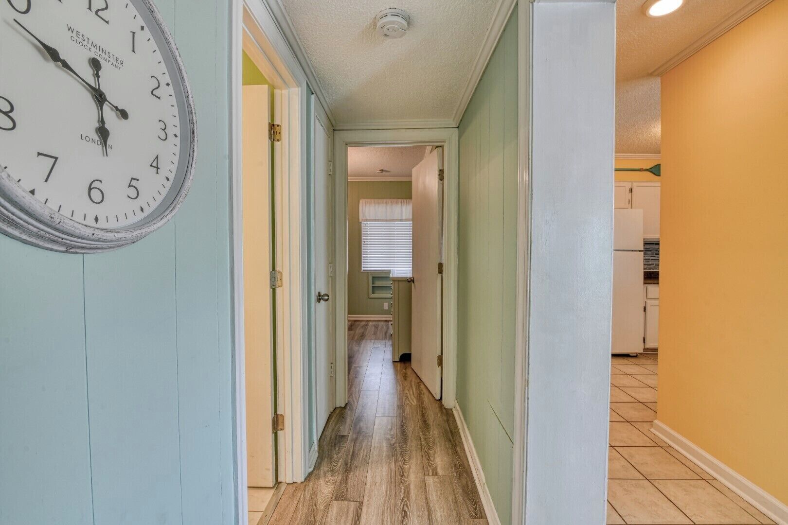 A hallway with a clock on the left, leading to a kitchen area.