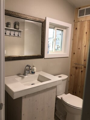 A bathroom with a white sink, a mirror, a window, and a wooden shower enclosure. - Bunglow in the Bend - 5 min walk to the beach (Grand Bend)