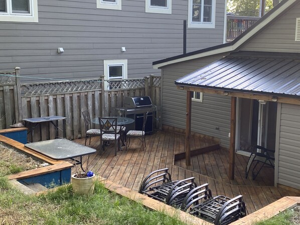 A backyard with a wooden deck, a barbecue grill, a table with chairs, and a covered patio area. - Bunglow in the Bend - 5 min walk to the beach (Grand Bend)