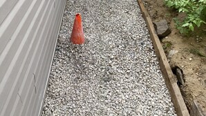 Un camí de grava que porta a un edifici amb una tanca de fusta i vegetació.