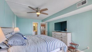 Un dormitorio con cama, ventilador de techo, televisión y cómoda.