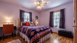 Ein Schlafzimmer mit Bett, Schreibtisch, Stuhl, Deckenventilator und einem Fenster mit Vorhängen.