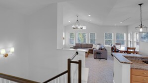 A spacious living area with a high ceiling, a staircase with a wooden handrail, and a kitchen with a granite countertop. - Beautiful resort condo with golf course views (Thornton)