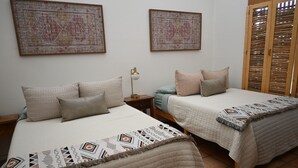 A bedroom with two beds, a nightstand, a lamp, and two wall-mounted paintings.