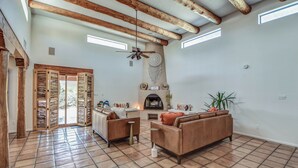 A spacious living room with a fireplace, wooden beams, and a ceiling fan.