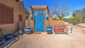 A desert-style building with a blue door, a red bench, and potted cacti.