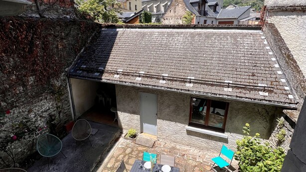 A courtyard with a stone table and chairs, a small garden, and a view of a mountain and church in the background. - Beautiful renovated apartment with courtyard (Bagnères-de-Luchon)