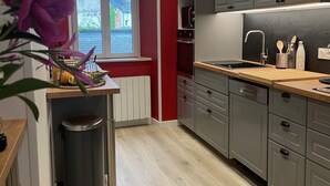 A modern kitchen with grey cabinets, a wooden countertop, and a window with a view of a house. - Beautiful renovated apartment with courtyard (Bagnères-de-Luchon)