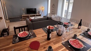 A dining area with a wooden table set for a meal, a television in the background, and a cozy living space with a sofa and a decorative birdcage. - Beautiful renovated apartment with courtyard (Bagnères-de-Luchon)