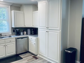 A kitchen with white cabinets, a coffee maker, a coffee pot, and a trash can.