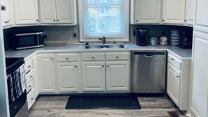 A kitchen with white cabinets, a stainless steel sink, a microwave, and a dishwasher. - Historic Pursuit of Happyness (Gastonia)
