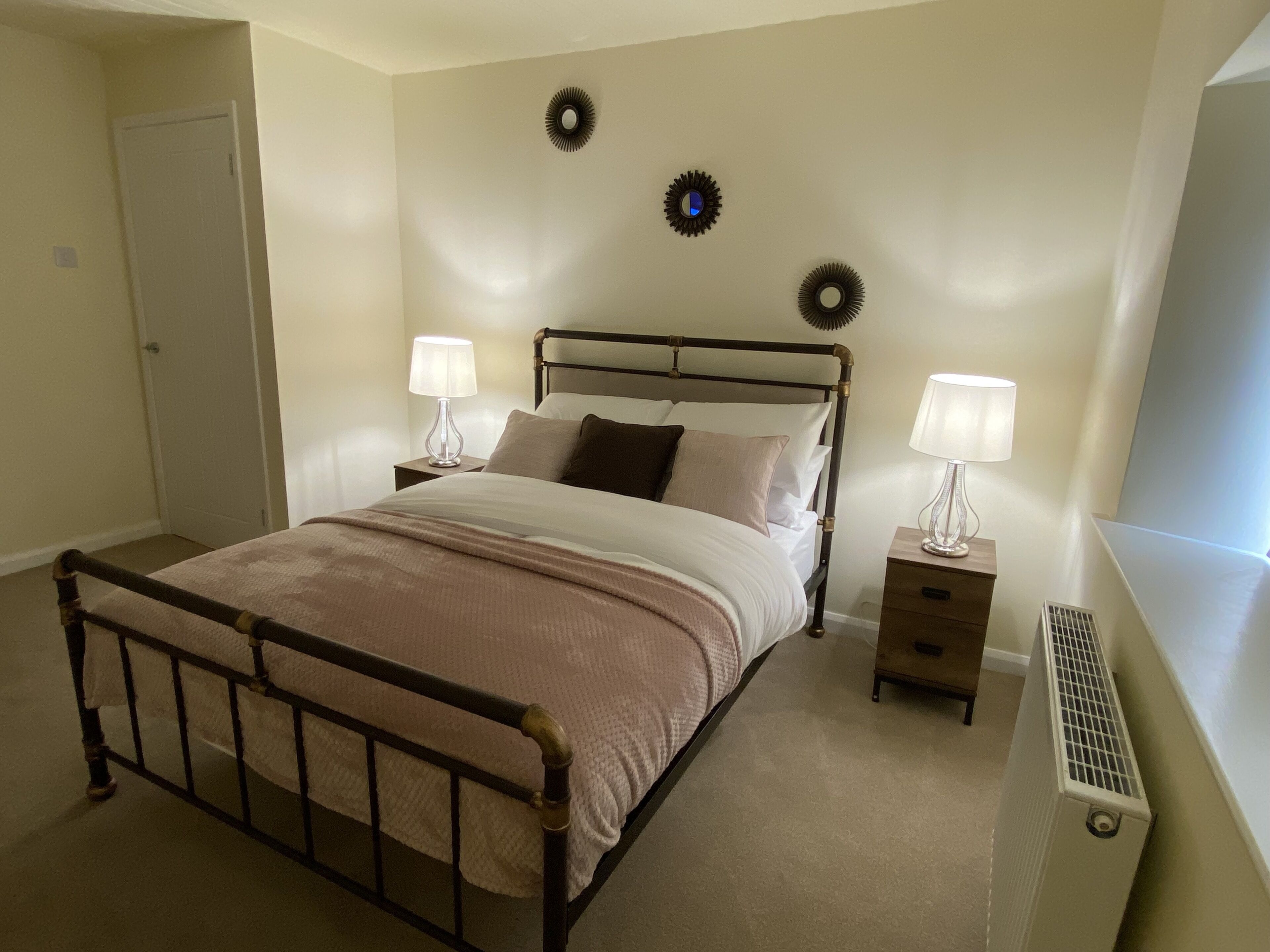 A bedroom with a bed, two bedside tables with lamps, a radiator, and decorative wall plates.