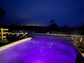 A rooftop pool with a purple-lit edge, surrounded by a stone wall and a wooden fence.