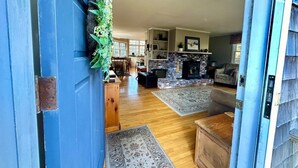 A cozy living room with a fireplace, wooden flooring, and a dining area in the background.