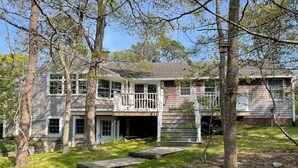 A two-story house with a porch, surrounded by trees.