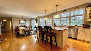A spacious kitchen with wooden flooring, a central island with bar stools, and large windows providing natural light.