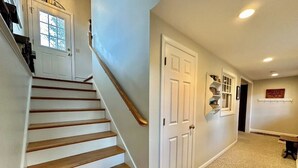 A hallway with a wooden staircase, white doors, and a carpeted floor.