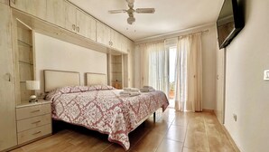 Ein Schlafzimmer mit einem Bett, einem Nachttisch, einem Deckenventilator und einem an der Wand befestigten Fernseher.