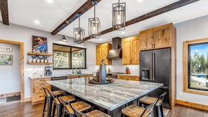A spacious kitchen with a large island, wooden cabinets, and a stainless steel refrigerator. - Brand New Construction! Ski-In/Ski-Out Townhome with Private Hot Tub! (Whitefish)