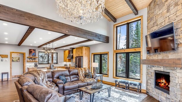 A spacious living room with a large leather sofa, a fireplace, and a stone wall. - Brand New Construction! Ski-In/Ski-Out Townhome with Private Hot Tub! (Whitefish)