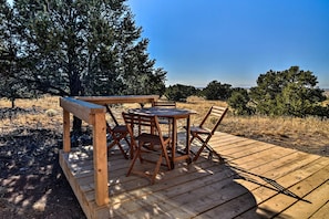 Eine Holzterrasse mit Tisch und Stühlen, umgeben von Bäumen und blauem Himmel.
