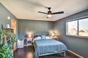 Ein Schlafzimmer mit einem Bett, zwei Nachttischen, einem Deckenventilator, einem Fenster und einer Pflanze.