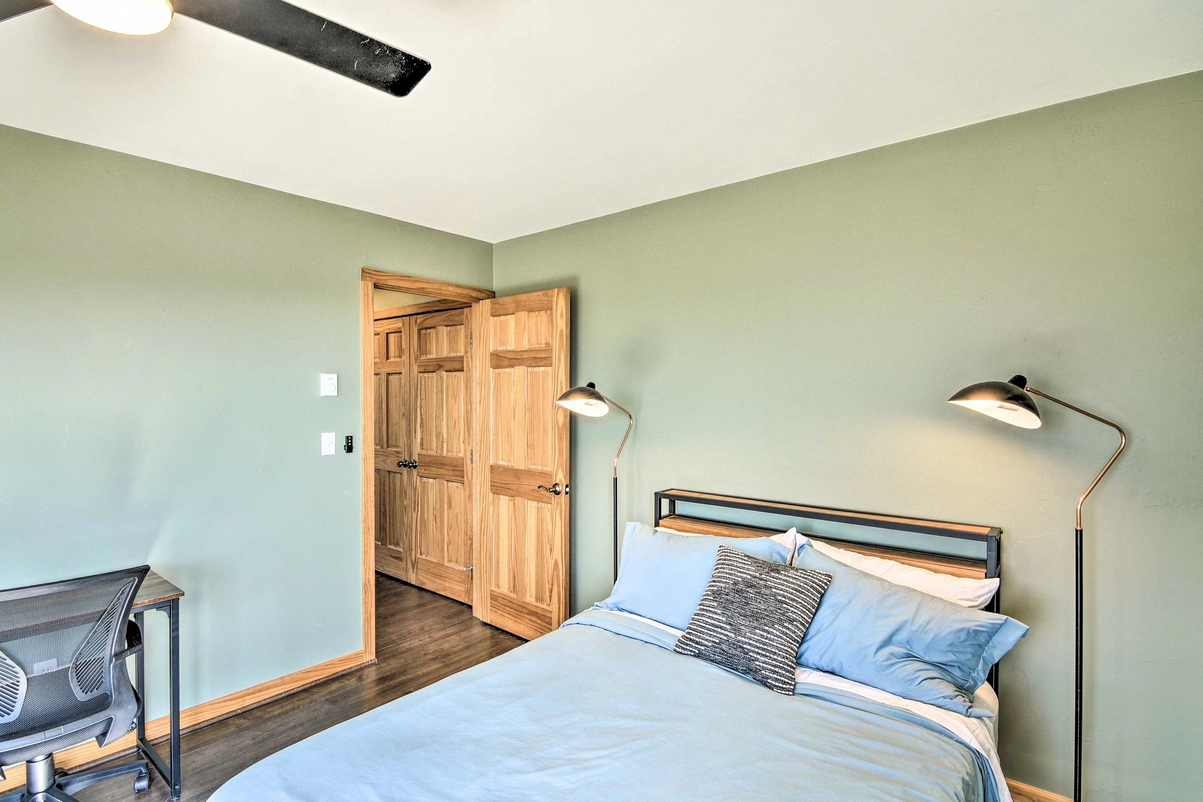 Une chambre à coucher comprenant un lit, des lampes de chevet, un bureau avec une chaise et une armoire en bois.