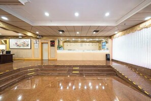 Een hotellobby met een receptiebalie, een digitale klok en een groot raam.