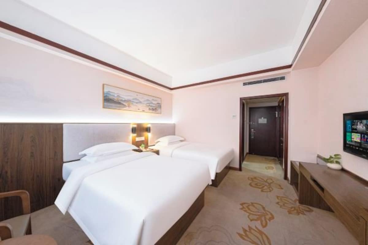 A hotel room with two beds, a desk, a television, and a door leading to another room.