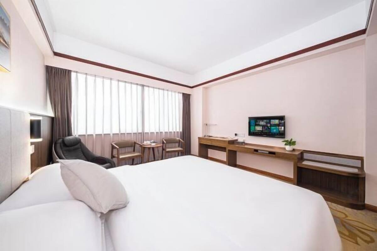 A hotel room with a large bed, a desk, a chair, a TV, and a window with curtains.