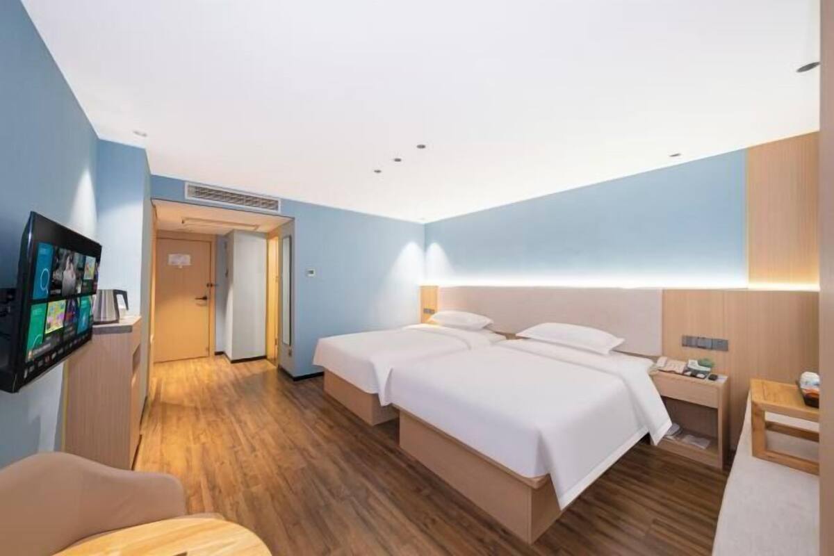 A hotel room with a bed, bedside table, TV, and wooden flooring.