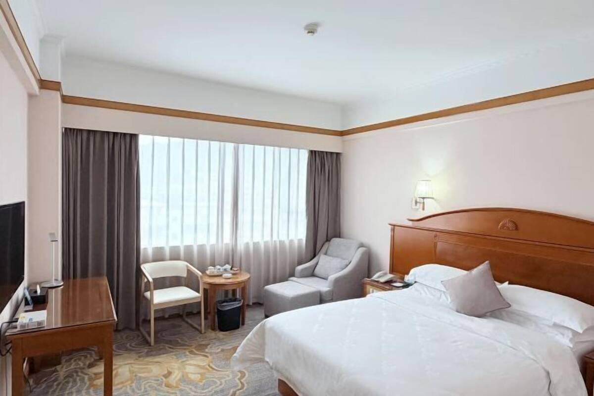 A hotel room with a bed, a desk, a chair, a small table, and a TV.