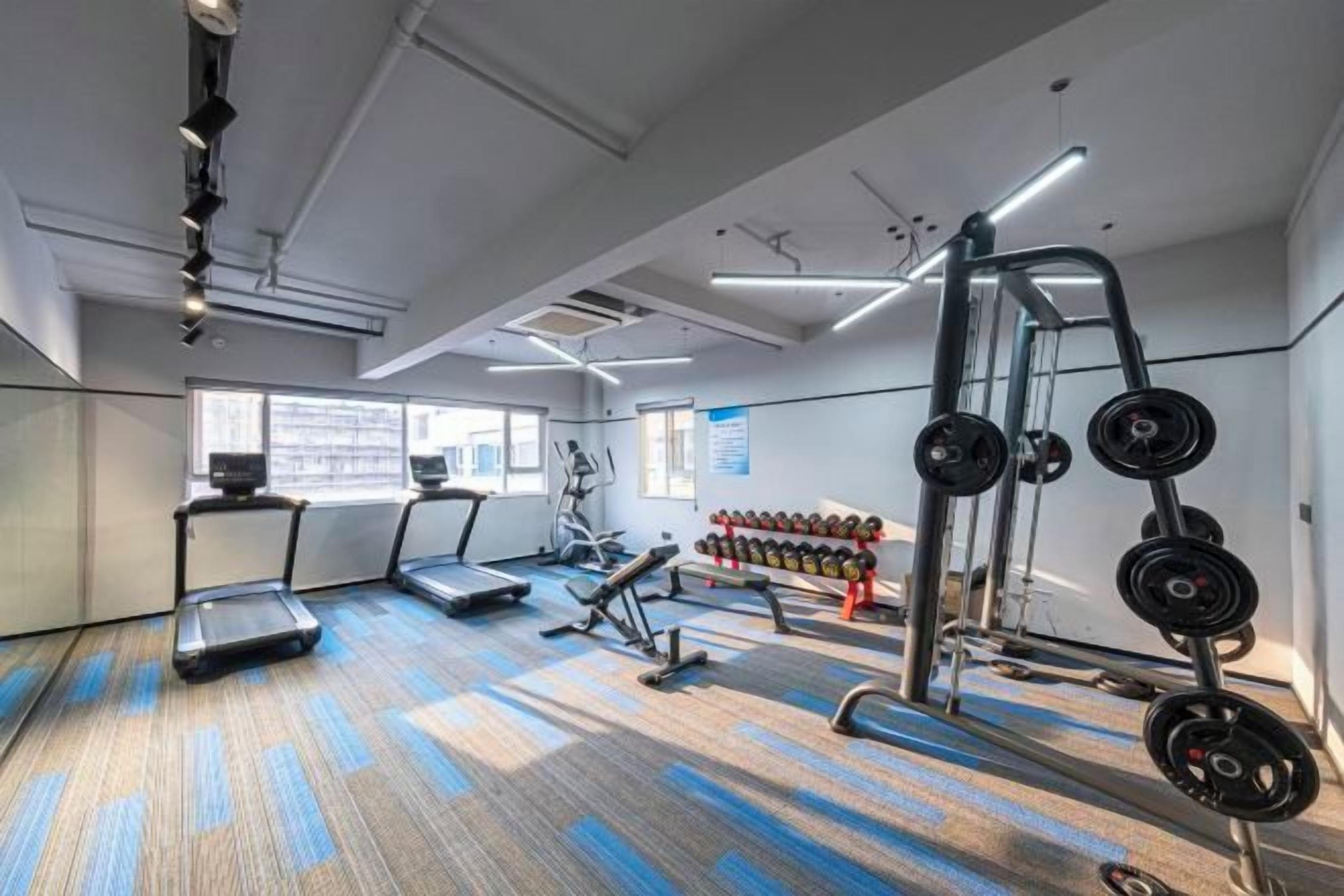 Un gimnasio con cintas de correr, equipamiento de levantamiento de pesas y mancuernas.