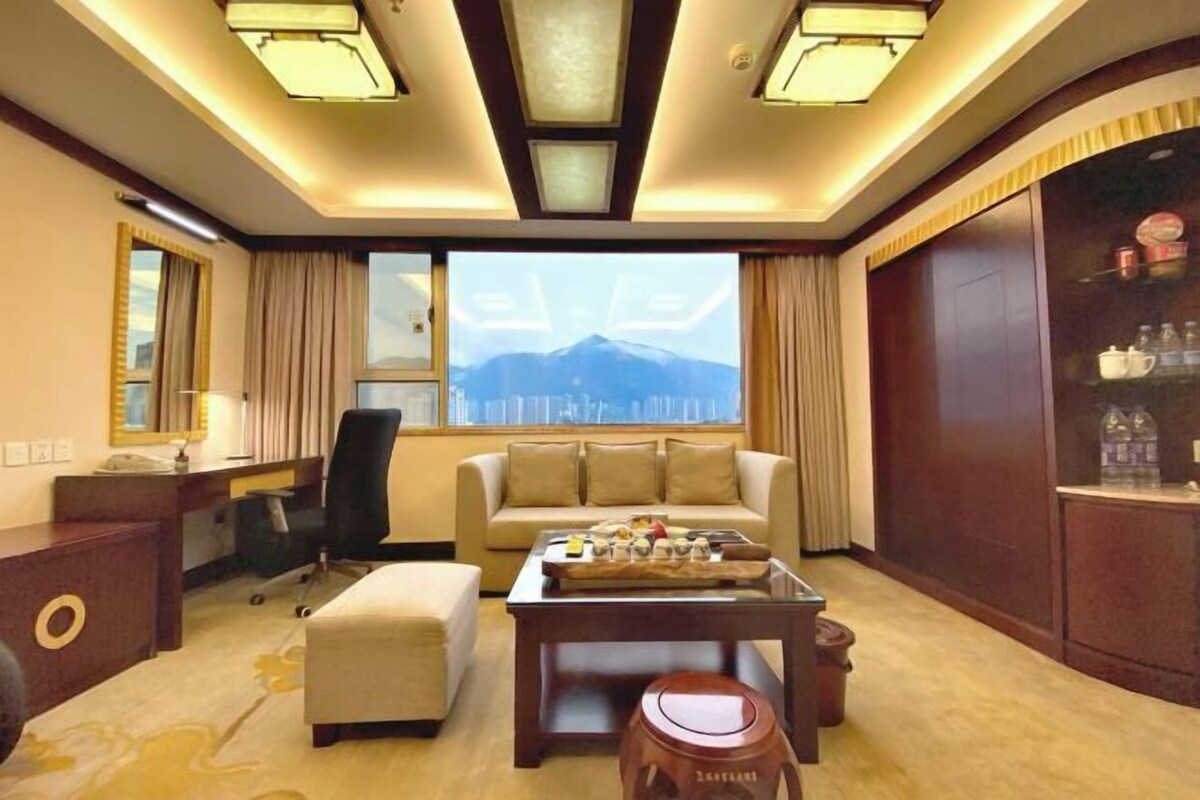 A hotel room with a sofa, a coffee table, a desk, and a view of mountains through the window.