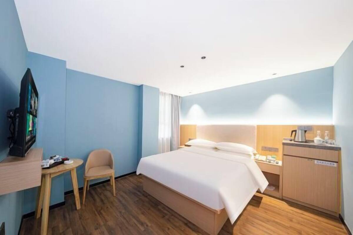 A hotel room with a bed, a desk, a chair, a TV, and a small table.