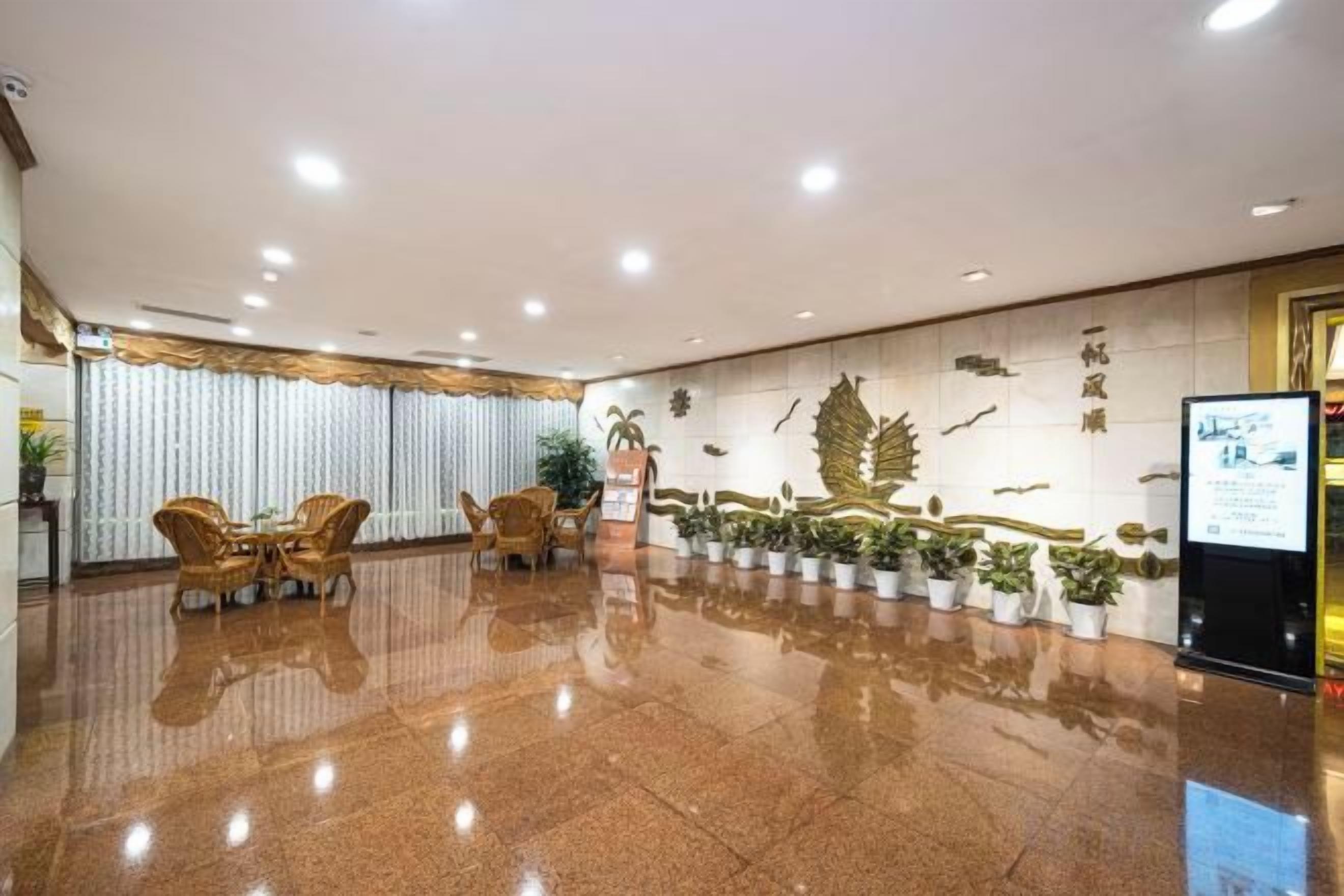 A hotel lobby with a polished floor, seating area, potted plants, and a wall with decorative elements.