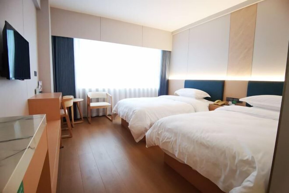 A hotel room with two beds, a desk, a chair, and a television.