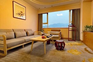 A modern hotel room with a sofa, a small table, and a chair. There is a window with a view of the mountains.