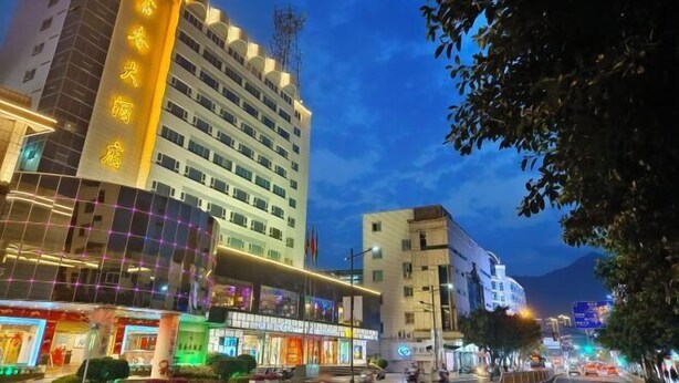 A multi-story hotel with illuminated signage, a modern facade, and a bustling street scene in the background. - Fuchun Hotel (Fu'an)