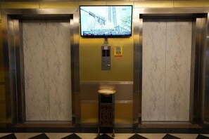 An elevator interior with a television screen displaying a news broadcast, a small wooden stool, and a safety sign. - Fuchun Hotel (Fu'an)