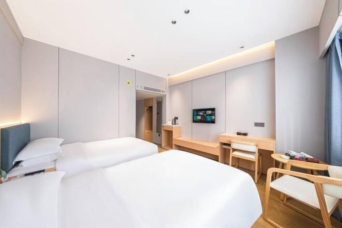 A modern hotel room with two beds, a desk, a chair, and a TV.
