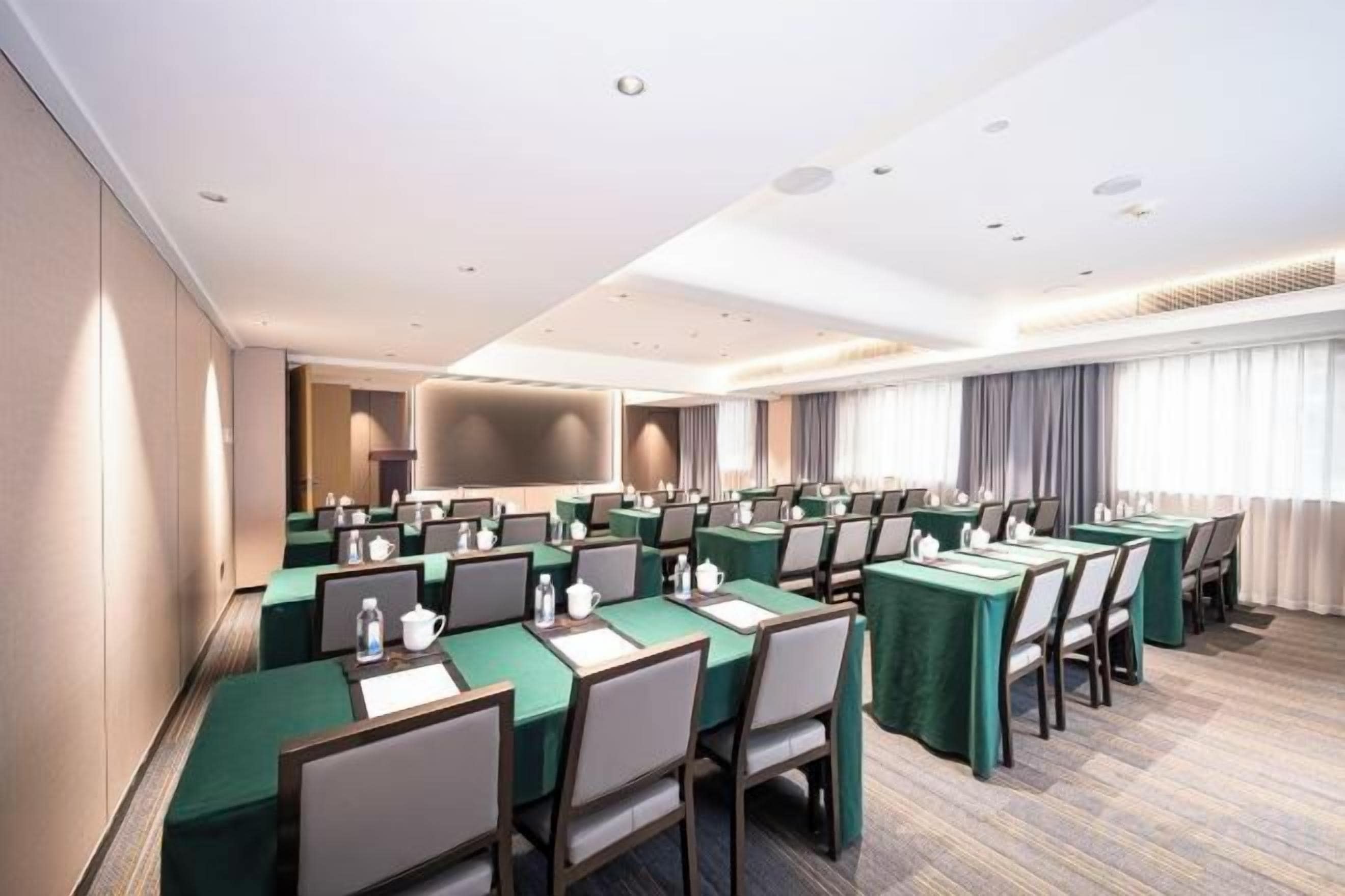 A conference room with multiple tables, chairs, and a large screen.