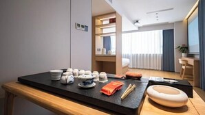 A modern hotel room with a dining area featuring a black table, white and blue ceramic dishes, and a wooden bench. - Fuchun Hotel (Fu'an)