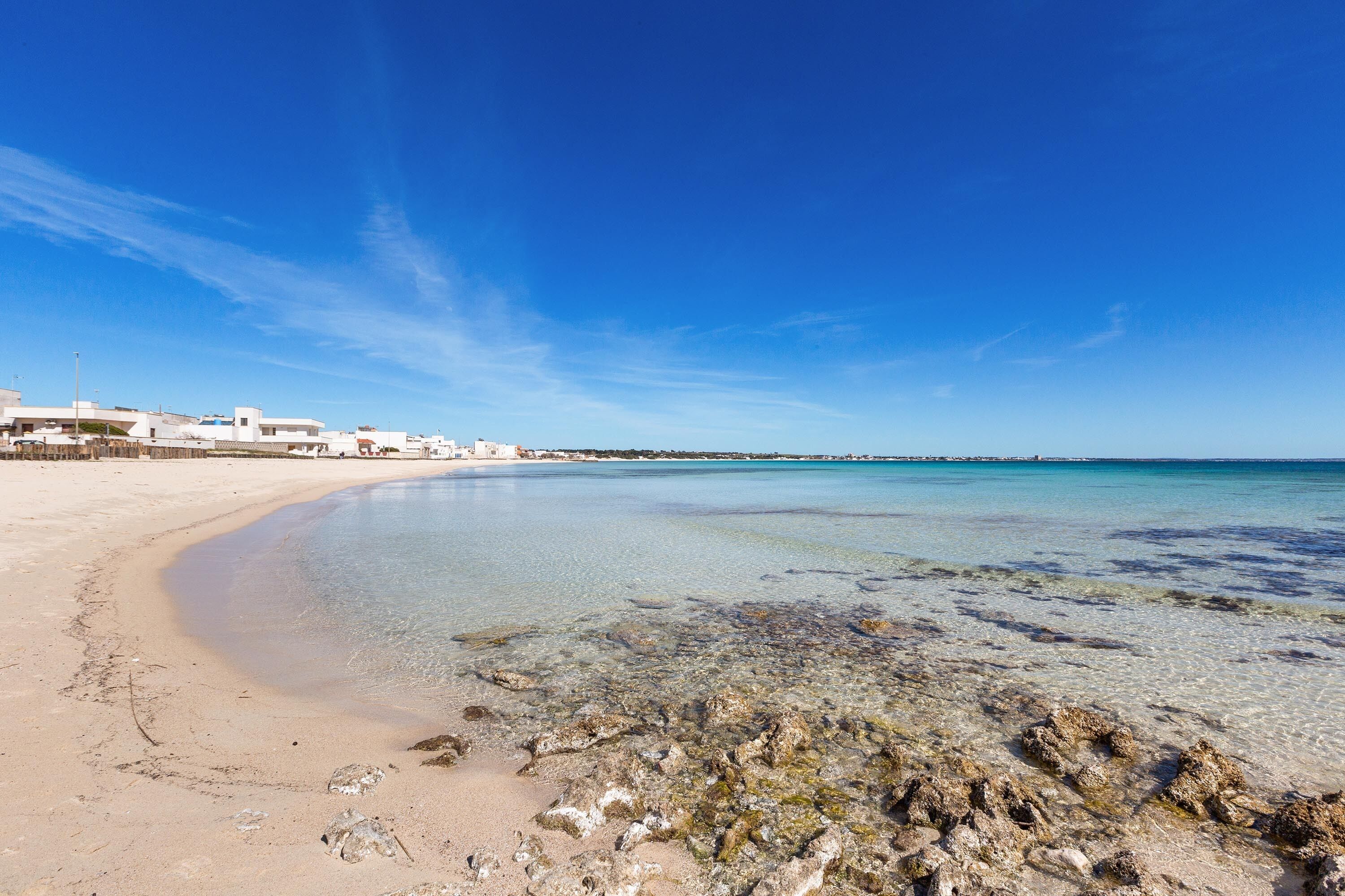 Une plage avec une eau claire, un rivage sablonneux et des bâtiments en arrière-plan.