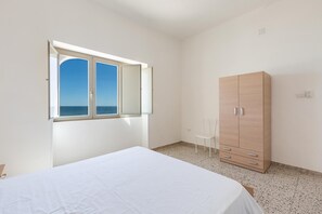 Une chambre à coucher comprenant un lit, une armoire, une chaise et une fenêtre donnant sur la mer.