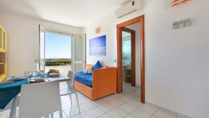 A modern living room with a sofa, dining table, and chairs. There is a large window providing a view of the outdoors. - Residence Punta Cassano - Fronte Mare PP (Melendugno)