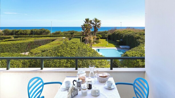 A balcony with a table set for tea, overlooking a pool and lush greenery. - Residence Punta Cassano - Fronte Mare PP (Melendugno)