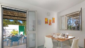 Ein Essbereich mit einem Tisch für vier Personen, weißen Stühlen und Blick durch eine Glastür auf eine Terrasse.